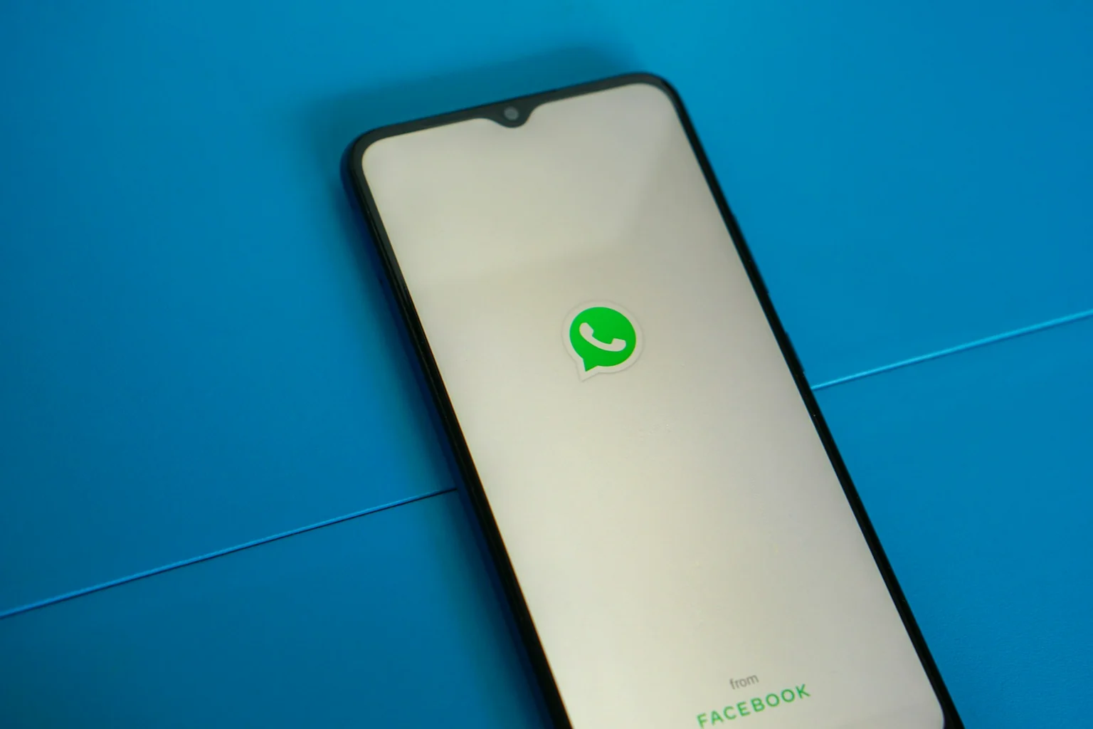 Celular sobre uma mesa azul com o logotipo do WhatsApp na tela.